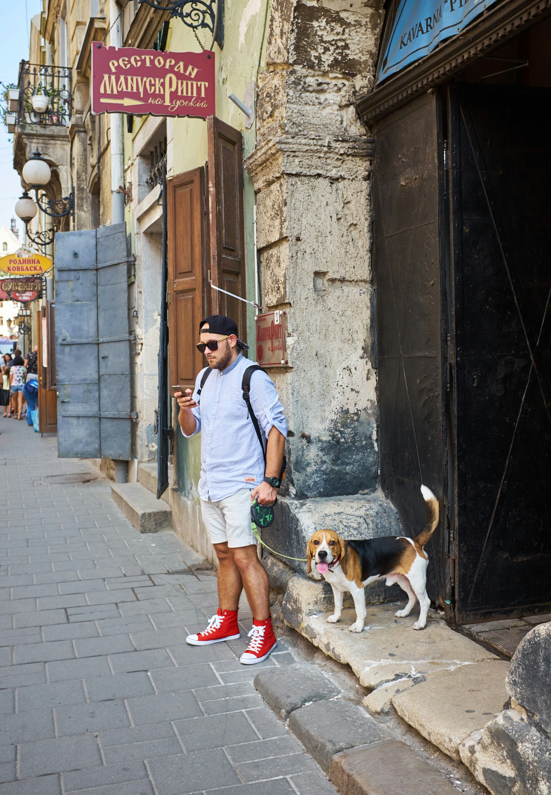 Man in casual outfit standing on the street with a beagle on a leash beside an old building