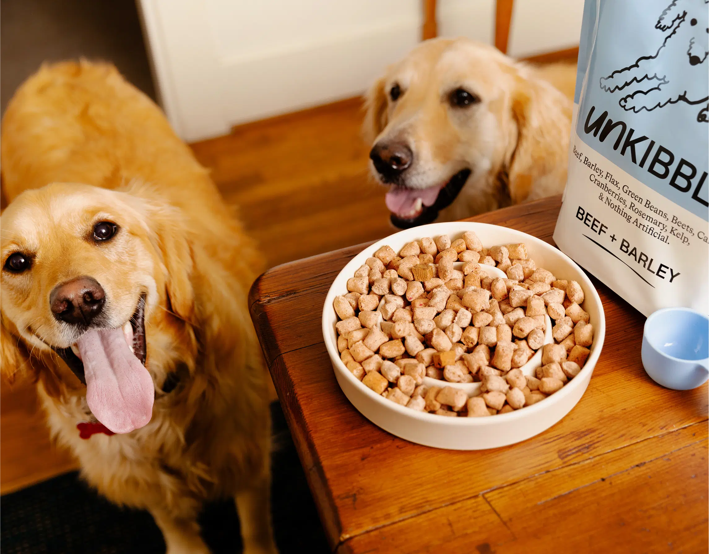 Two happy Golden Retrievers with a bowl of Spot & Tango UnKibble beef and barley recipe, a fresh dry dog food alternative.