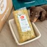 Mini dachshund lies next to a turkey recipe meal pack from The Farmer’s Dog on a wooden floor beside branded delivery items.