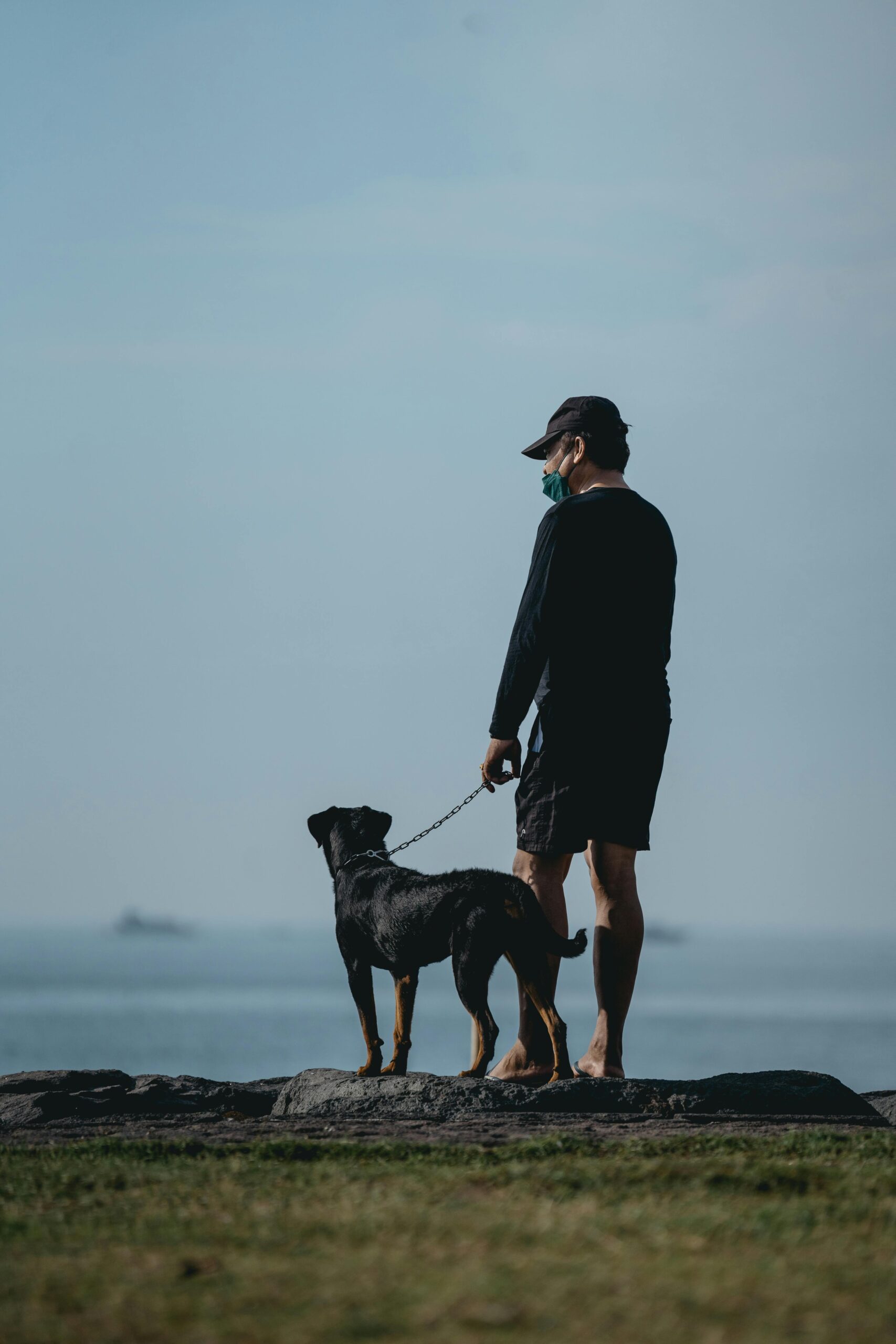 Man walking barefoot with a leashed Rottweiler by the ocean.