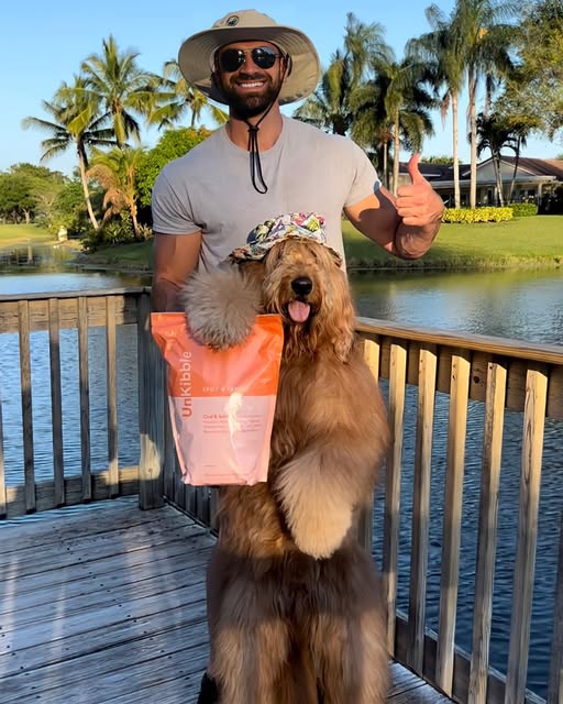 Man and Goldendoodle dog posing on a wooden dock holding a bag of Spot & Tango UnKibble Chicken & Sweet Potato