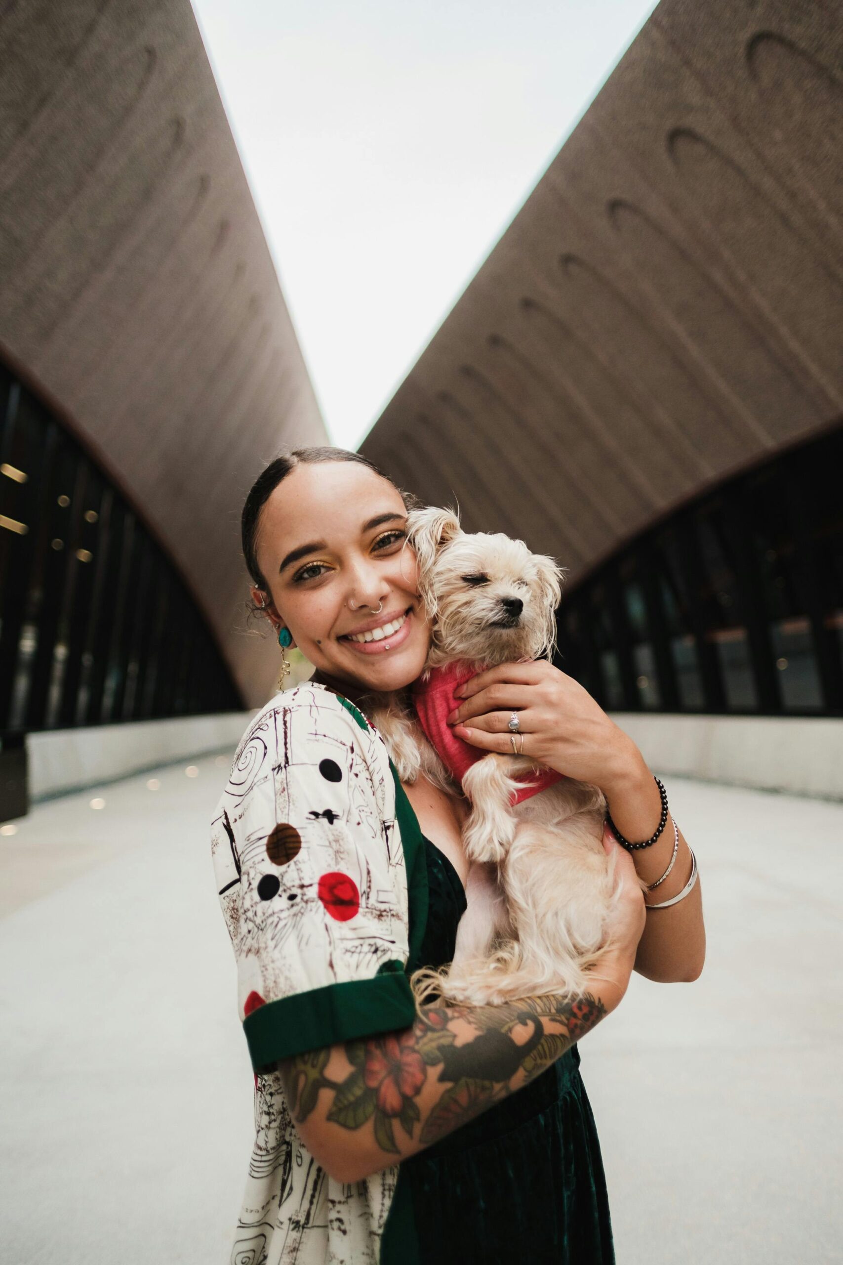 Young woman smiling and holding a Yorkshire Terrier wearing a red sweater, posing in an urban outdoor space